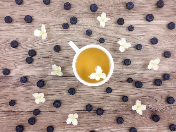 Taza de té verde caliente, flores y bayas en la mesa de madera. Puesta plana — Foto de Stock