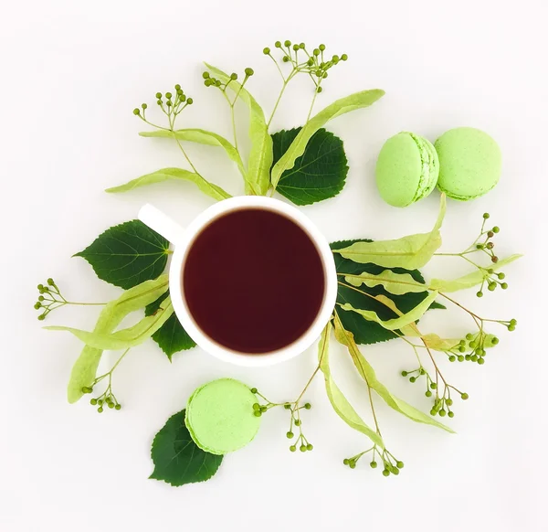 Macarrones verdes brillantes y taza de té decorado con flores sobre fondo blanco. Puesta plana —  Fotos de Stock