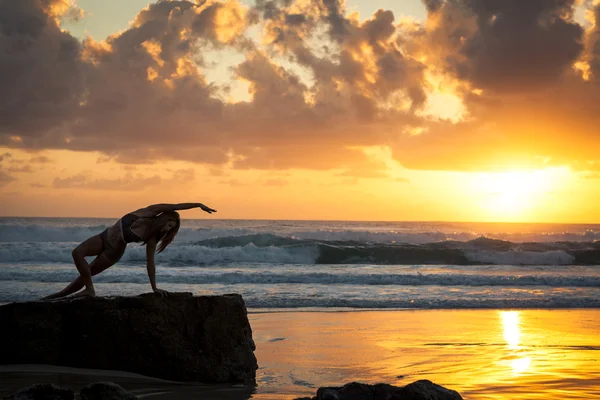 Donna in forma che si estende sulla spiaggia all'alba — Foto Stock