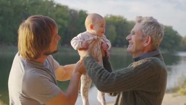 Üç nesildir erkekler. Büyükbaba, baba ve küçük torun. Gün batımı, nehrin kıyısında.. — Stok video