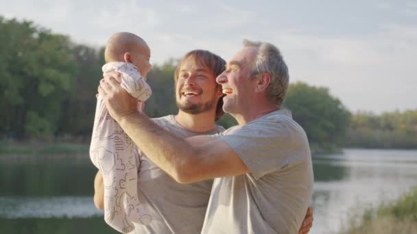 Tres generaciones de hombres. Abuelo, padre y nieto. Puesta de sol, la orilla del río. — Vídeo de stock