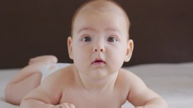 Güzel, gülümseyen bebek: Yatağa uzanmış güzel, küçük bir bebek kameraya gülümsüyor..