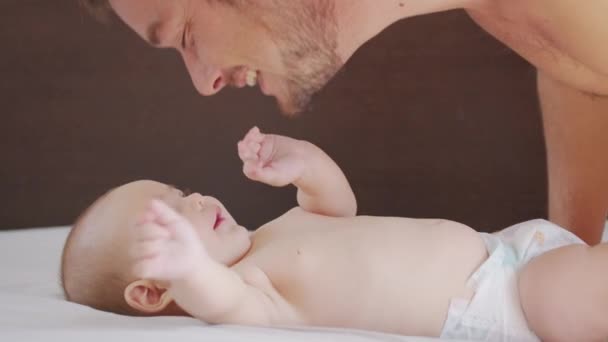 Nahaufnahme. Der Vater küsst das Baby sanft und genießt die liebevolle Mutter, die sich zu Hause spielerisch um das Kleinkind kümmert und die Verbindung mit ihrem Neugeborenen teilt. Gesunde Kinderbetreuung. — Stockvideo