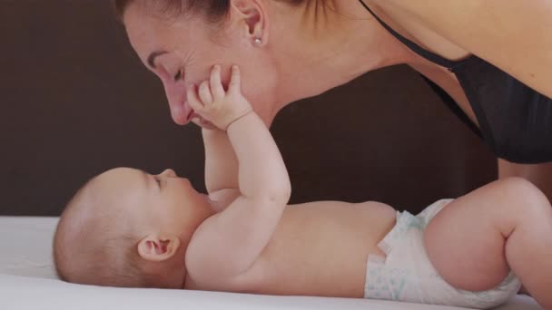 穿上衣服母亲温柔地亲吻着爱抚着孩子的母亲，在家里开玩笑地照顾着幼儿，与新生的孩子分享着联系。健康儿童保育. — 图库视频影像