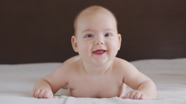 Güzel, gülümseyen bebek: Yatağa uzanmış güzel, küçük bir bebek kameraya gülümsüyor..