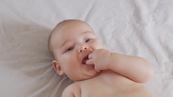 Kleine baby met vinger in de mond op een bed. — Stockvideo