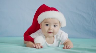 Mutlu Noeller ve mutlu yıllar, çocukluk, tatil konsepti yakın çekim. Noel Baba şapkalı yeni doğmuş 3 aylık bebek karnında emekliyor..