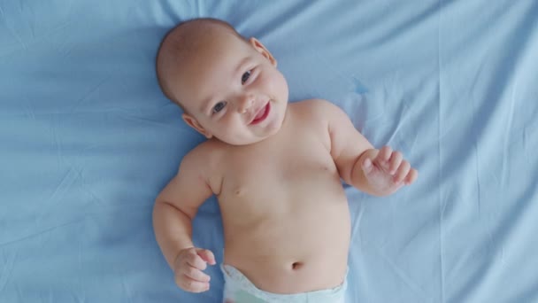 Egy kedves kis kaukázusi újszülött vicces mosollyal a hátán fekszik. Portré egy játékos és energikus gyerekről közelkép. — Stock videók
