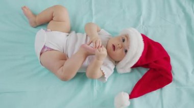 2021 'de gülümseyen komik küçük bebek. Noel Baba şapkası takan tatlı çocuk kanepede yatıyor..
