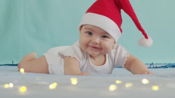 Lustigt litet barn som ler. Söta spädbarn pojke bär Santa hatt liggande på soffan. — Stockvideo