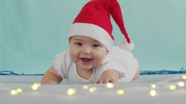 Um bebé engraçado a sorrir. Bonito menino usando chapéu de Papai Noel deitado no sofá. — Vídeo de Stock