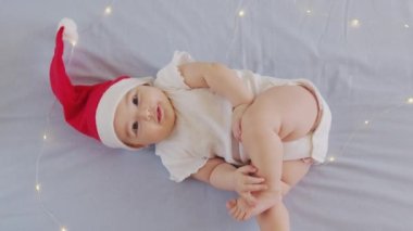 2021 'de gülümseyen komik küçük bebek. Noel Baba şapkası takan tatlı çocuk kanepede yatıyor..