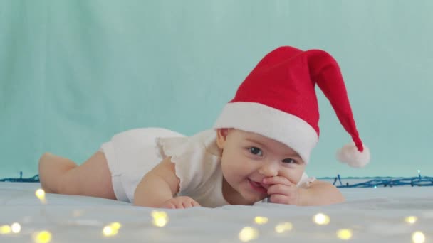 Lustigt litet barn som ler. Söta spädbarn pojke bär Santa hatt liggande på soffan. — Stockvideo
