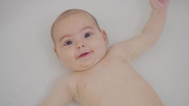 Kafkasyalı yeni doğmuş güzel bir bebek komiktir, sırıtır, banyoda arkada yatar. Neşeli ve enerjik bir çocuğun portresi.