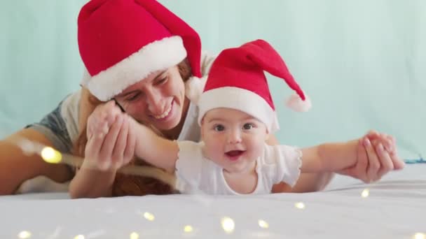 Uśmiechnięte dziecko Santa leżące w stroju Świętego Mikołaja, w czerwonym kapeluszu z matką. — Wideo stockowe
