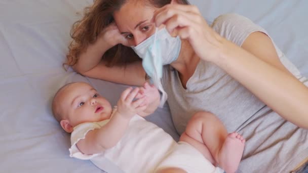 Mam probeert een medisch masker voor haar dochtertje. Coronavirus of COVID-19. Schattig klein meisje met een beschermend masker thuis. — Stockvideo