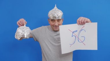 Yaşlı adamın elinde 5G işareti olmayan bir levha var. 5G teknolojisini ve 5G uyumlu anten konuşlandırmasını protesto ederken mavi arka planda duruyor..