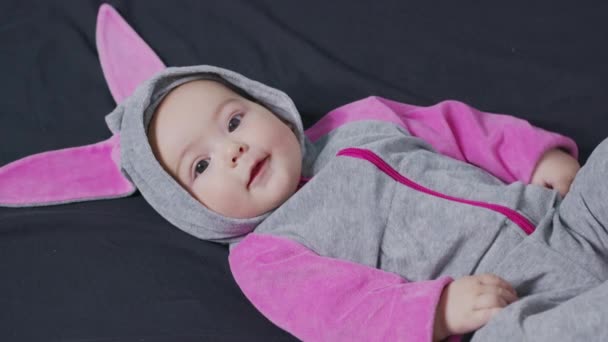 Χαριτωμένο μωρό χαμογελά και κοιτάζοντας στην κάμερα από κοντά. Μικρό παιδί με στολή κουνελιού, κορυφαία άποψη. — Αρχείο Βίντεο