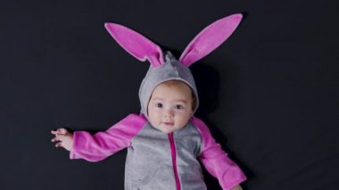 Sevimli bebek gülümsüyor ve kameraya yakından bakıyor. Paskalya tavşanı kostümü giymiş küçük bir çocuk..