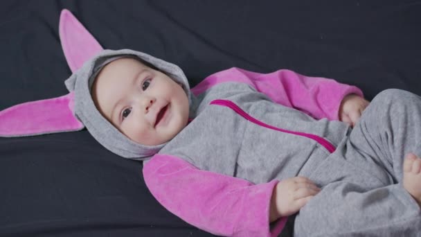 Lindo bebé sonriendo y mirando a la cámara de cerca. Niño pequeño en traje de conejito, vista superior. — Vídeos de Stock