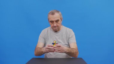 Rubik 'i çözen yaşlı bir adam. Mavi üzerine izole edilmiş..