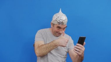 Alüminyum folyo şapkalı korkmuş adam 5G dalgalarından el salladı. 5G kule radyasyon koruması. Var olmayan bir soruna karşı mantıksız bir korku. Uzaylılardan beyne koruyucu folyo miğferi.