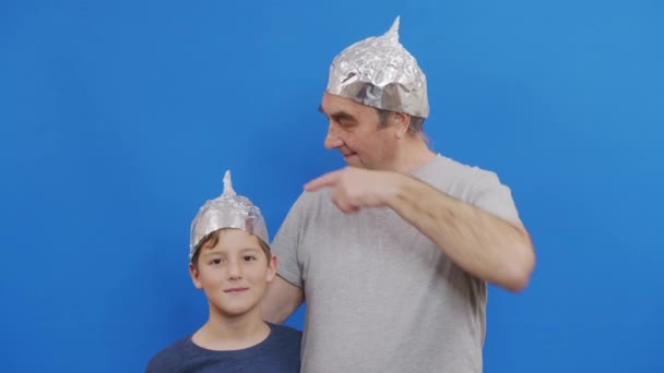 Abuelo con su nieto en sombreros de lámina protectora de la radiación 5g de pie sobre un fondo azul. — Vídeos de Stock