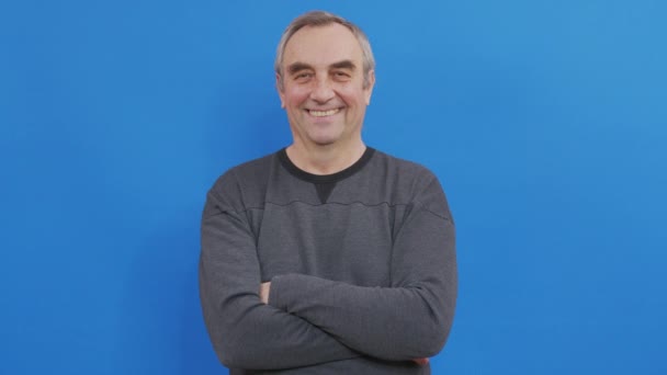 Retrato del anciano emocional sonriendo. Primer plano hombre maduro con emoción positiva. Hombre feliz con el pelo gris mirando hacia atrás. Aislado en azul. — Vídeos de Stock