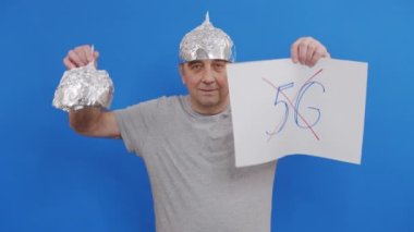 Elinde 5 G işareti olmayan bir pankart tutan adam. 5G teknolojisini ve 5G uyumlu anten konuşlandırmasını protesto ederken mavi arka planda duruyor..
