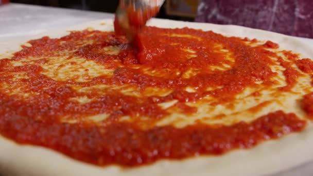 Close Up of Chef está extendiendo salsa de tomate en masa de pizza con una cuchara de metal en la tradicional pizza italiana. — Vídeo de stock