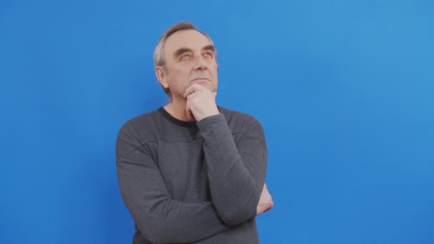 Tænker ældre mand ser op og rundt på blå baggrund. Bekymrede kontemplative ansigtsudtryk. Flot mandlig model. – Stock-video