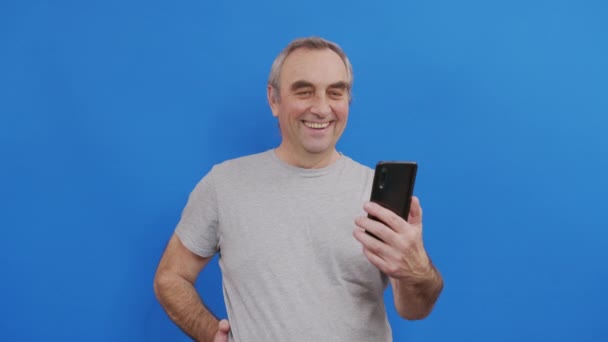 스마트폰을 들고 온라인에서 화면을 보는 휴대폰 동영상을 보고 있는 행복 한 노인. — 비디오