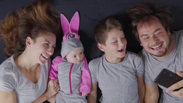 Famiglia felice con i suoi figli stanno facendo un selfie o una videochiamata a padre o parenti in un letto. Concetto di tecnologia, nuova generazione, famiglia, connessione, genitorialità, autenticità. — Video Stock
