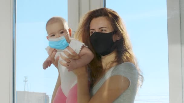 Femme avec bébé dans des masques de protection communique à travers la fenêtre en verre qui les sépare pendant la période de quarantaine stricte. — Video