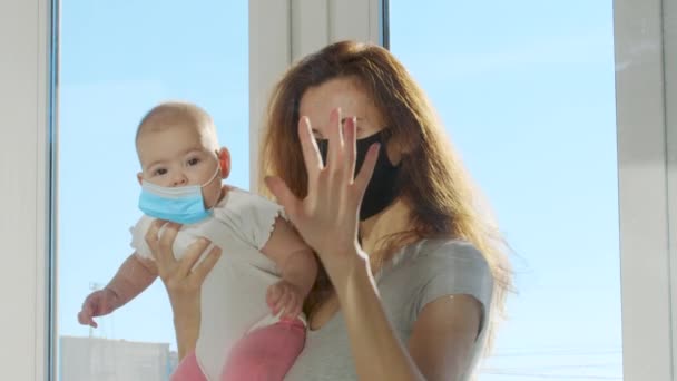 Жінка з дитиною в захисних масках спілкується через скляне вікно, яке відокремлює їх під час суворого карантину . — стокове відео