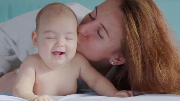 Sonriendo hermosa madre caucásica jugando con el bebé recién nacido en la cama en el dormitorio. Los padres y la linda infancia infantil se relajan y disfrutan juntos en casa. Concepto de familia feliz y cuidado del bebé. — Vídeo de stock