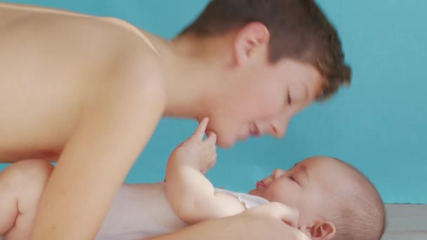 Pojke kysser nyfödd syster liggande tillsammans på sängen hemma. Porträtt av bedårande bebis och småbarn pojke syskon leka och koppla av. Begreppet barndom och familj. — Stockvideo