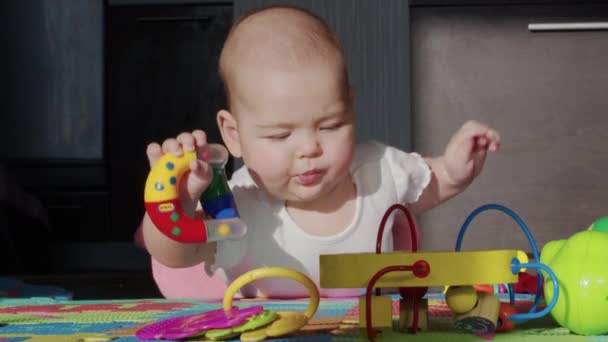 Grappig gelukkig baby meisje kruipt met speelgoed kinderziektes op de maag en zwaait op de knieën in fel zonlicht kinderdagverblijf. — Stockvideo