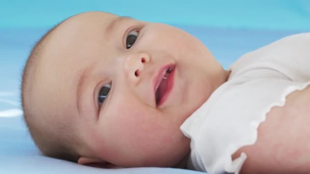 Ritratto ravvicinato di una bambina. La faccia di una ragazzina caucasica sdraiata sul letto. bambino 5 mesi guardando in macchina fotografica. — Video Stock