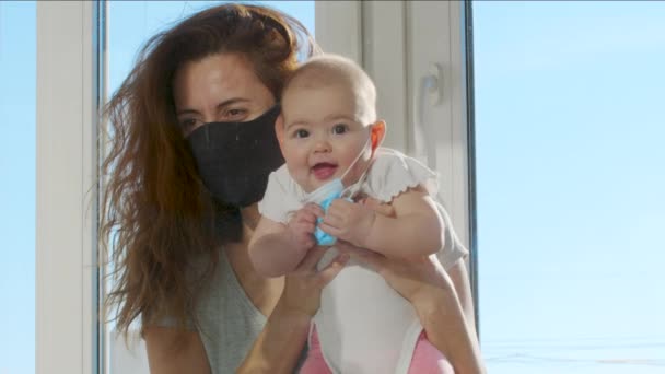 Mère dans le masque médical communiqué avec bébé sur les mains à travers la fenêtre en verre. Covid-19 personnes malades pandémiques en quarantaine. Rencontres en famille. Distance sociale. — Video