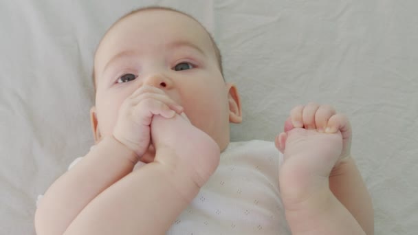 En liten pojke som leker med benen. Bit och sug hans tår. — Stockvideo