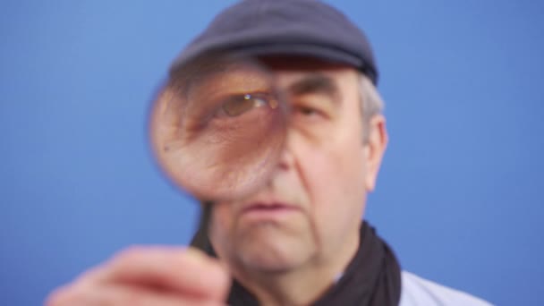 Забавный зрелый мужчина смотрит в камеру с увеличительным стеклом в поисках ценной информации. — стоковое видео