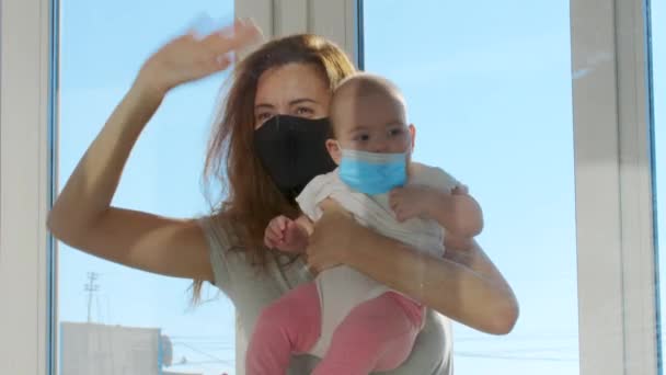 Mère dans le masque médical communiqué avec bébé sur les mains à travers la fenêtre en verre. Covid-19 personnes malades pandémiques en quarantaine. Rencontres en famille. Distance sociale. — Video