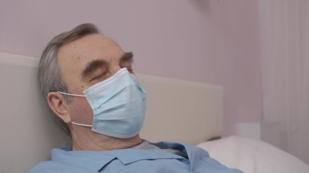 Triste malato anziano in isolamento a casa indossando una maschera di protezione del virus fatta a mano. — Video Stock