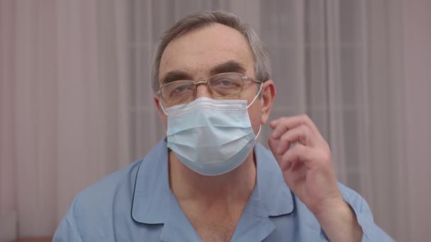 Κοντινό πορτρέτο ηλικιωμένος άνδρας βγάζει μια ιατρική μάσκα το πρόσωπό του. — Αρχείο Βίντεο