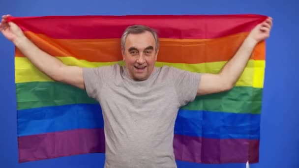 Homme âgé tenant le drapeau de la fierté de l'lgbt. Seule. Un seul. couvrant le drapeau LGBT. Drapeau LGBT sur fond bleu. — Video