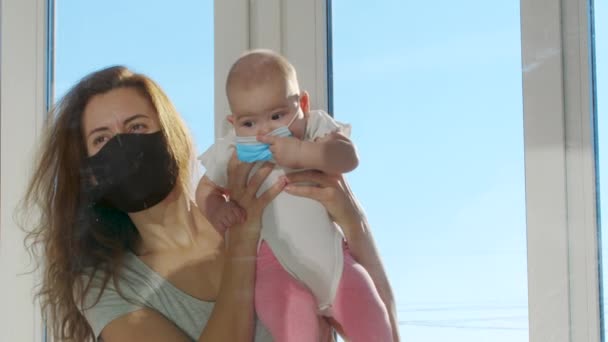 Femme avec bébé dans des masques de protection communique à travers la fenêtre en verre qui les sépare pendant la période de quarantaine stricte. — Video