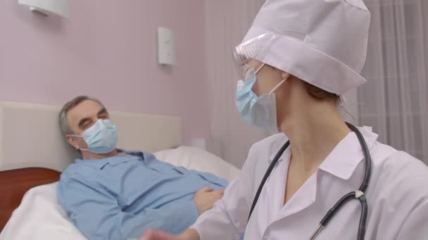 Близько кавказької жінки-лікаря рукою вимірювання температури пацієнтки середнього віку лежить на ліжку, страждаючи від Ковід-19 за допомогою інфрачервоного цифрового термометра.. — стокове відео