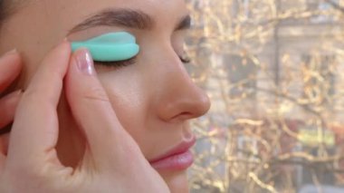 Profesyonel bir güzellik salonunda kirpik temizleme işlemi yapan genç bir kızın yüzü. Usta kirpik kıvırma işlemi sırasında kirpiklere özel bir fırçayla siyah boya sür.