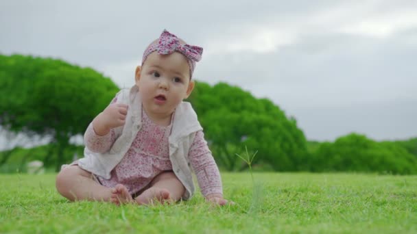 Engraçado bebê caucasiano está sentado em um gramado verde no parque. Aprendizagem e estudo do mundo ao redor. — Vídeo de Stock